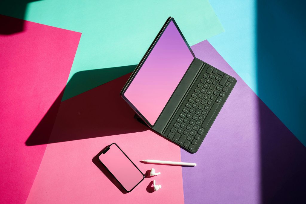 Tablet with keyboard, phone, stylus and earbuds laid out on bold colour-blocked paper