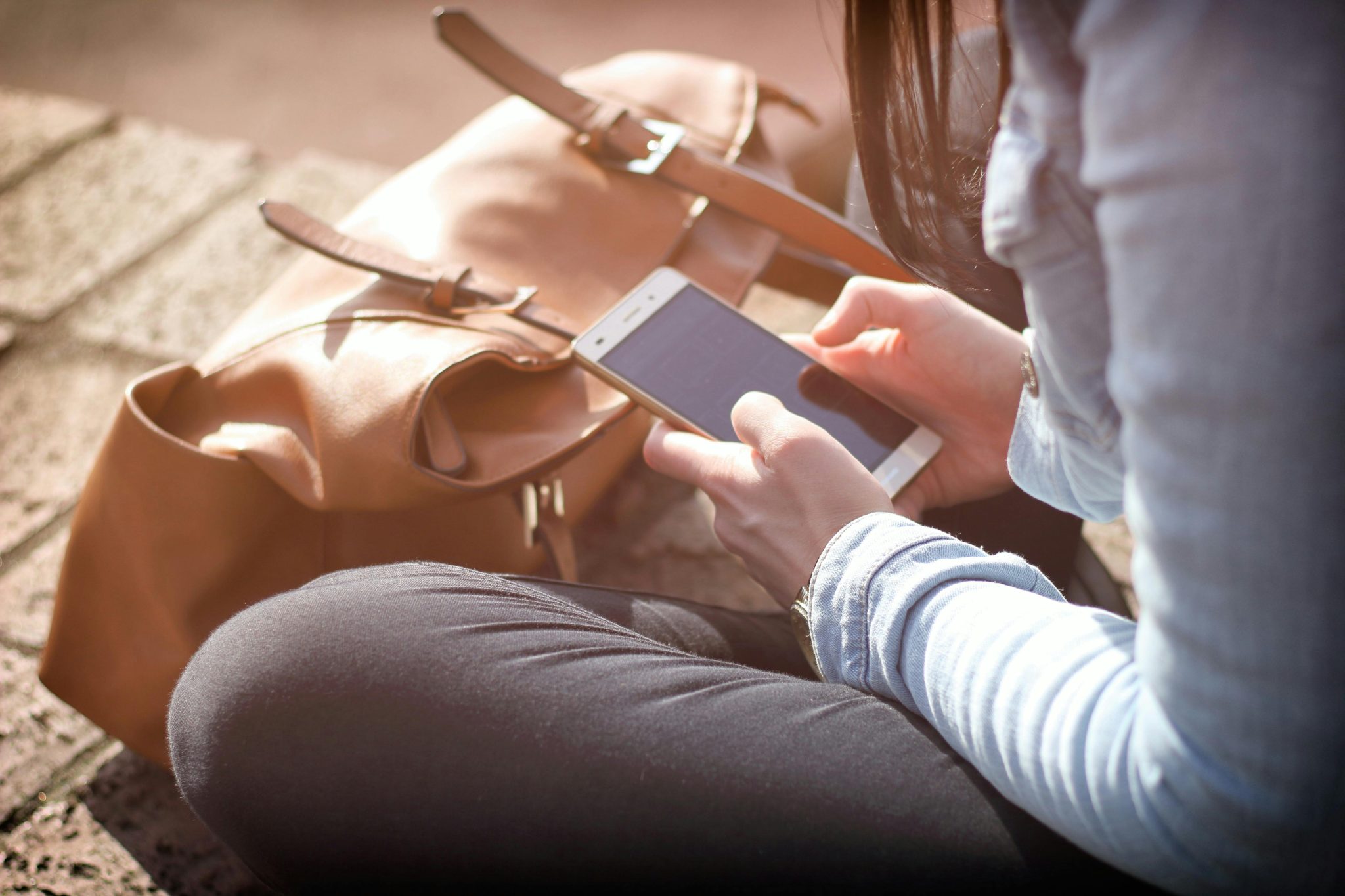 Someone sitting outdoors in the sun, using an app on their phone